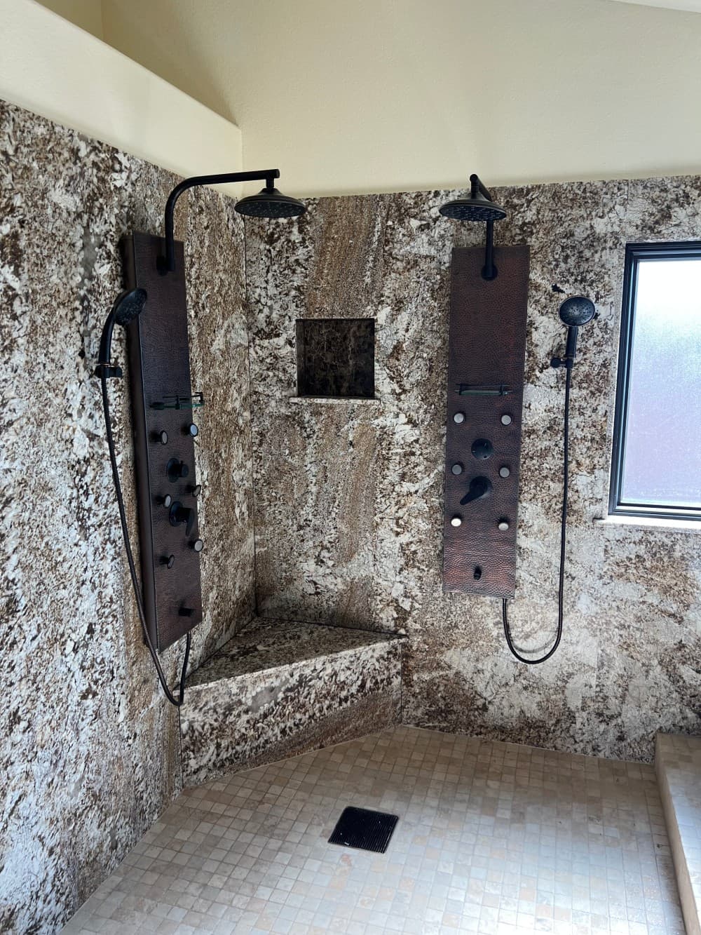 Custom walk-in shower with dual rainfall shower heads and travertine walls plumbed by Omnia Plumbing.